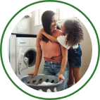A mother holds a laundry basket while her daughter hugs her from behind. 